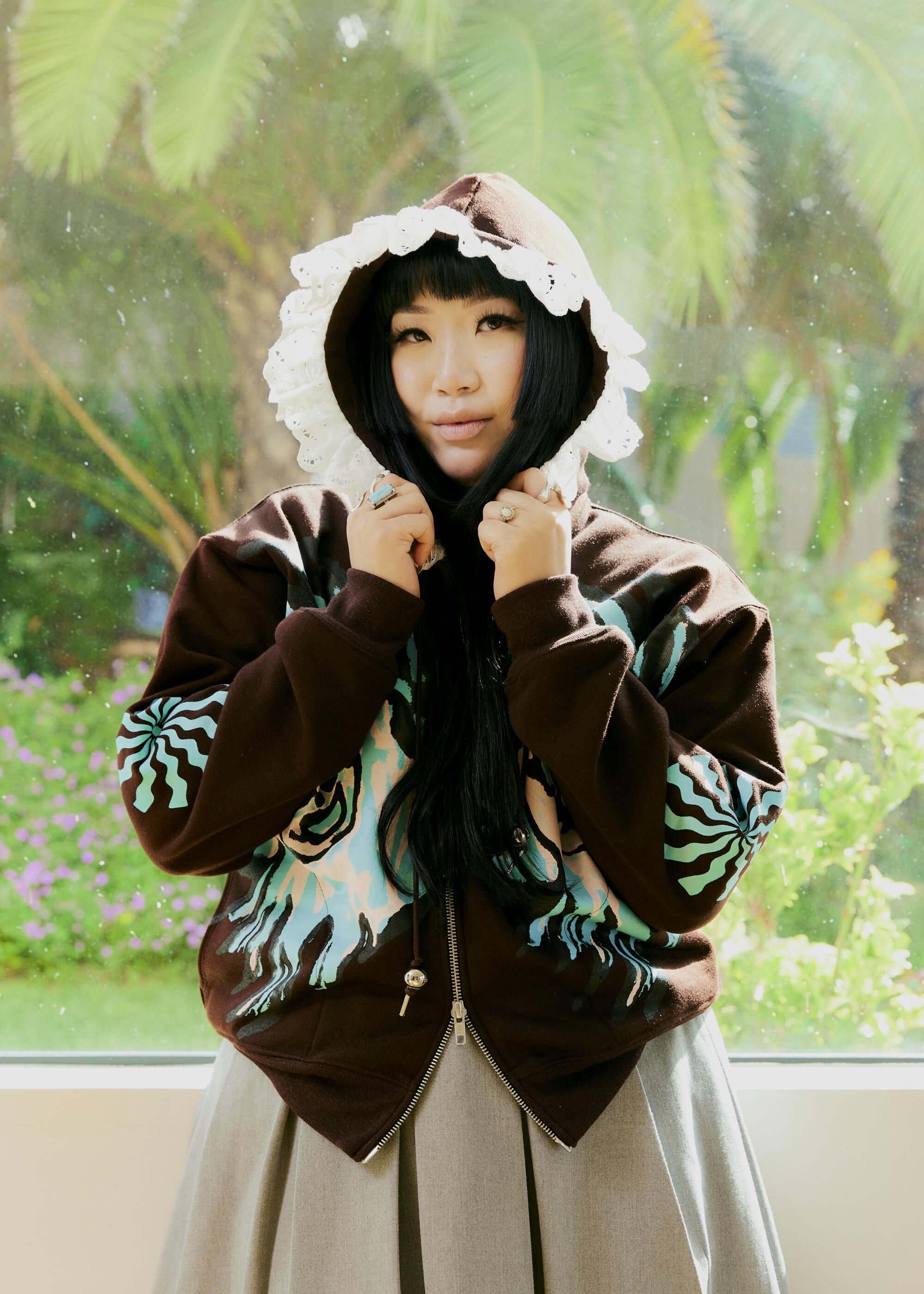 Stylist Jess Mori wearing a hoodie and plants in the background.
