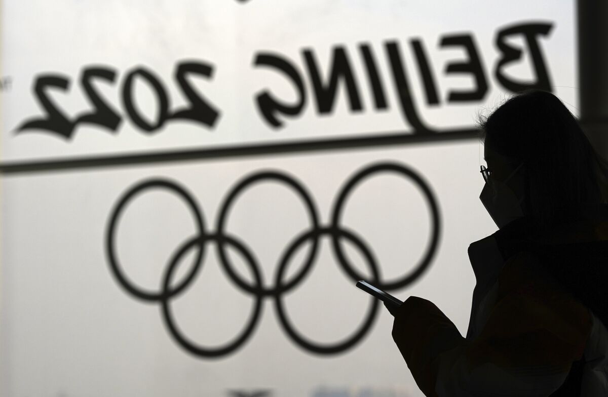 A woman looks at her phone as she passes an Olympic logo inside the main media center for the Beijing Winter Olympics Tuesday, Jan. 18, 2022, in Beijing. (AP Photo/David J. Phillip)