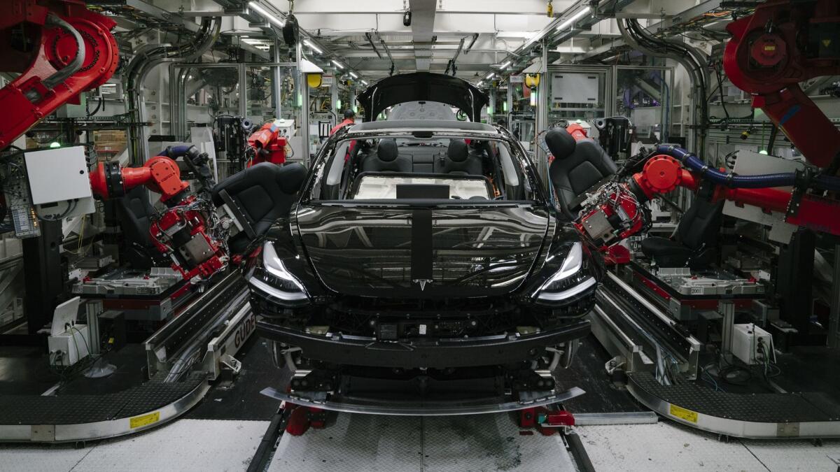Robotics arms install the front seats to a Tesla Model 3 at the company's factory in Fremont, Calif.