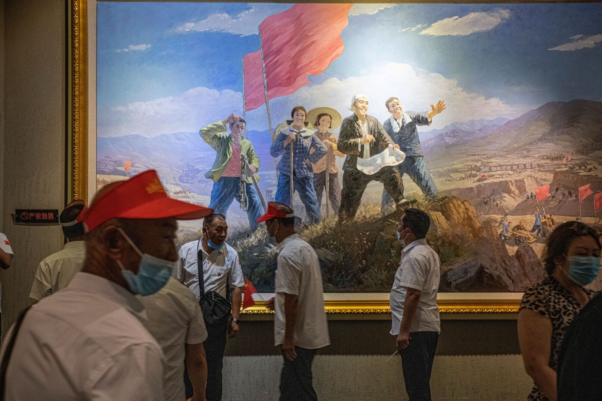 People stand before a large revolutionary-style painting depicting five people in a mountainous landscape and red flags