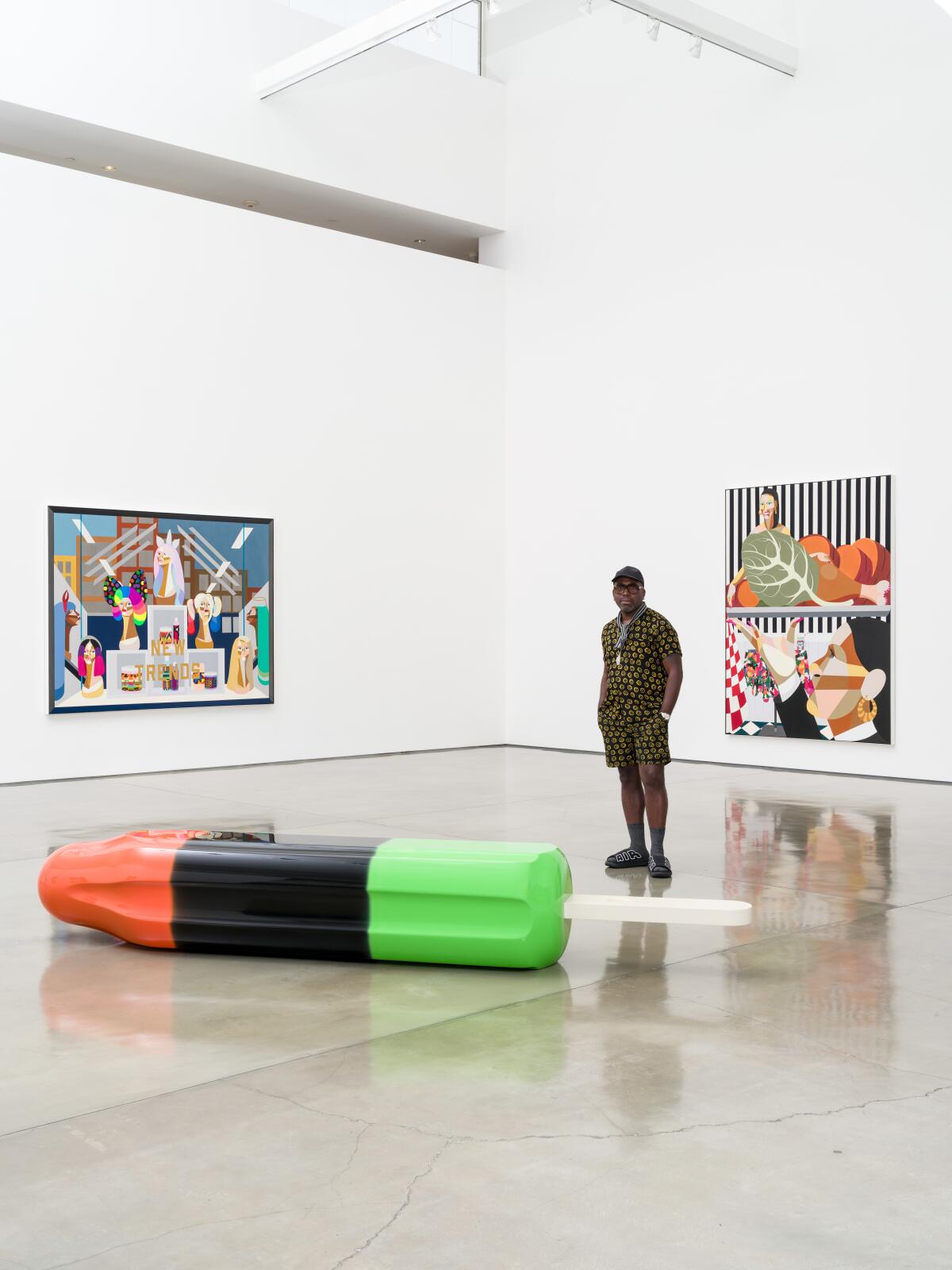 A man stands in an art gallery next to a giant popsicle sculpture on the floor