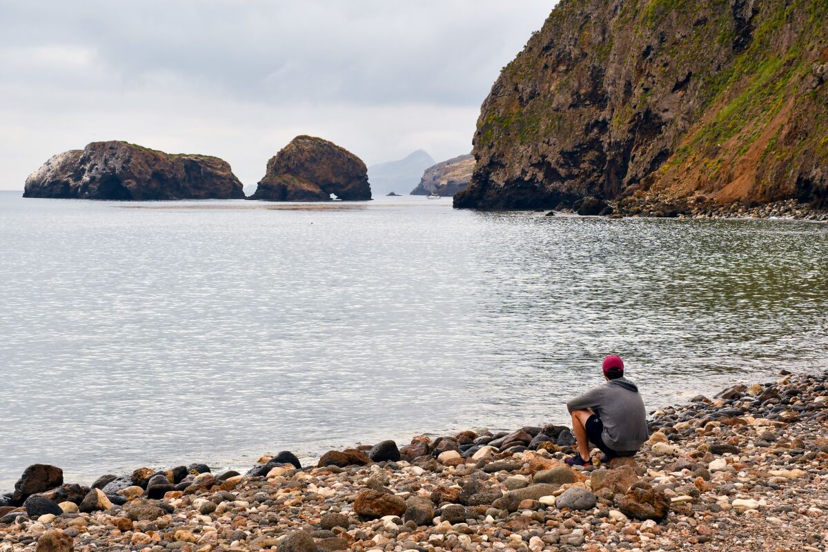 A person sits on a rocky beach in a cove.