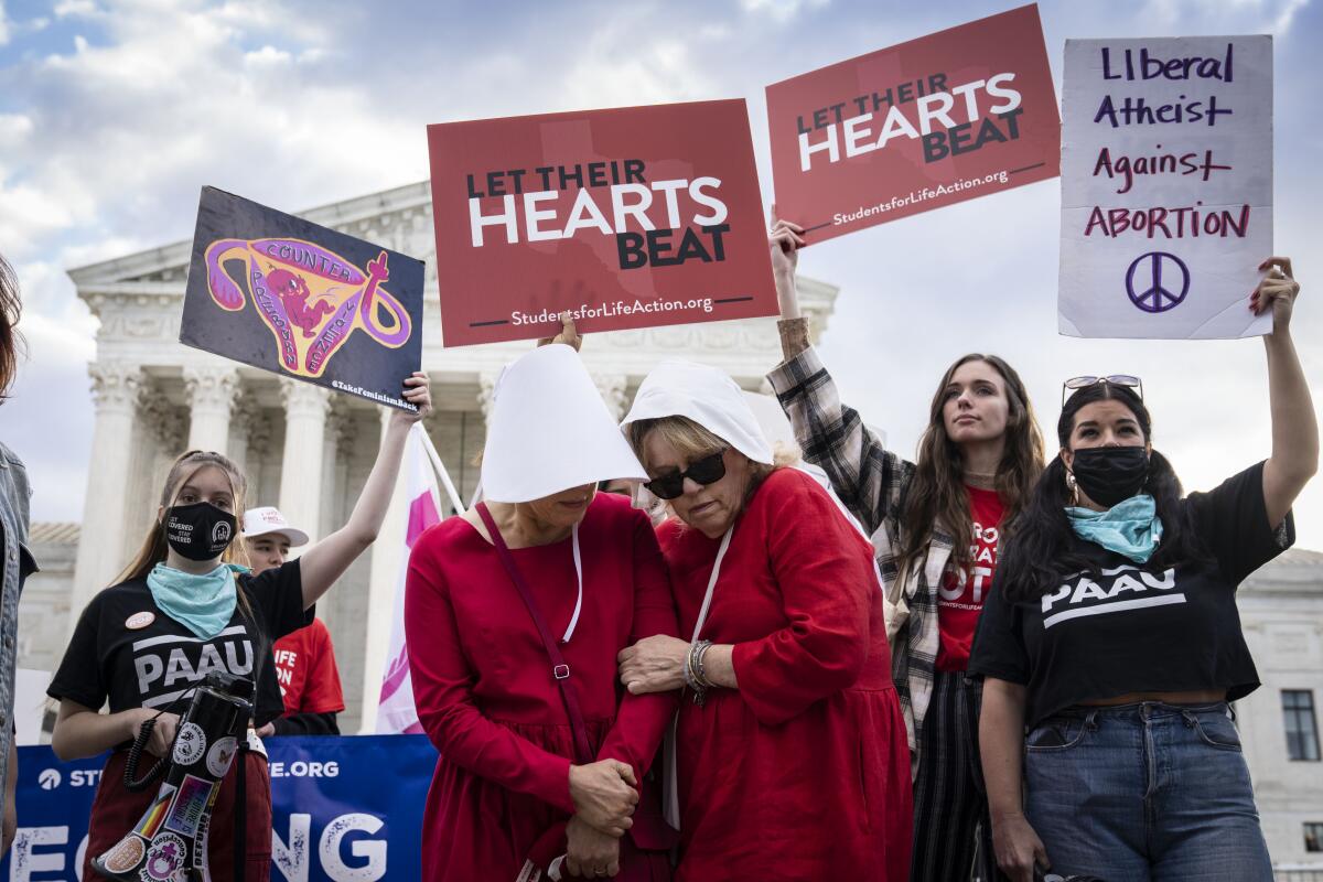 Two people in "Handmaid's Tale" costumes are surrounded by people holding antiabortion signs.