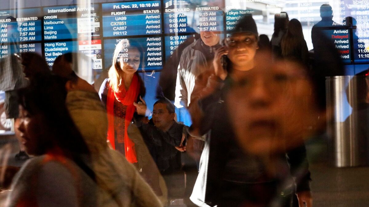 Travelers, reflected in sliding glass doors, take part in the Christmas getaway at the Tom Bradley International Terminal at Los Angeles International Airport on Dec. 22, 2017.