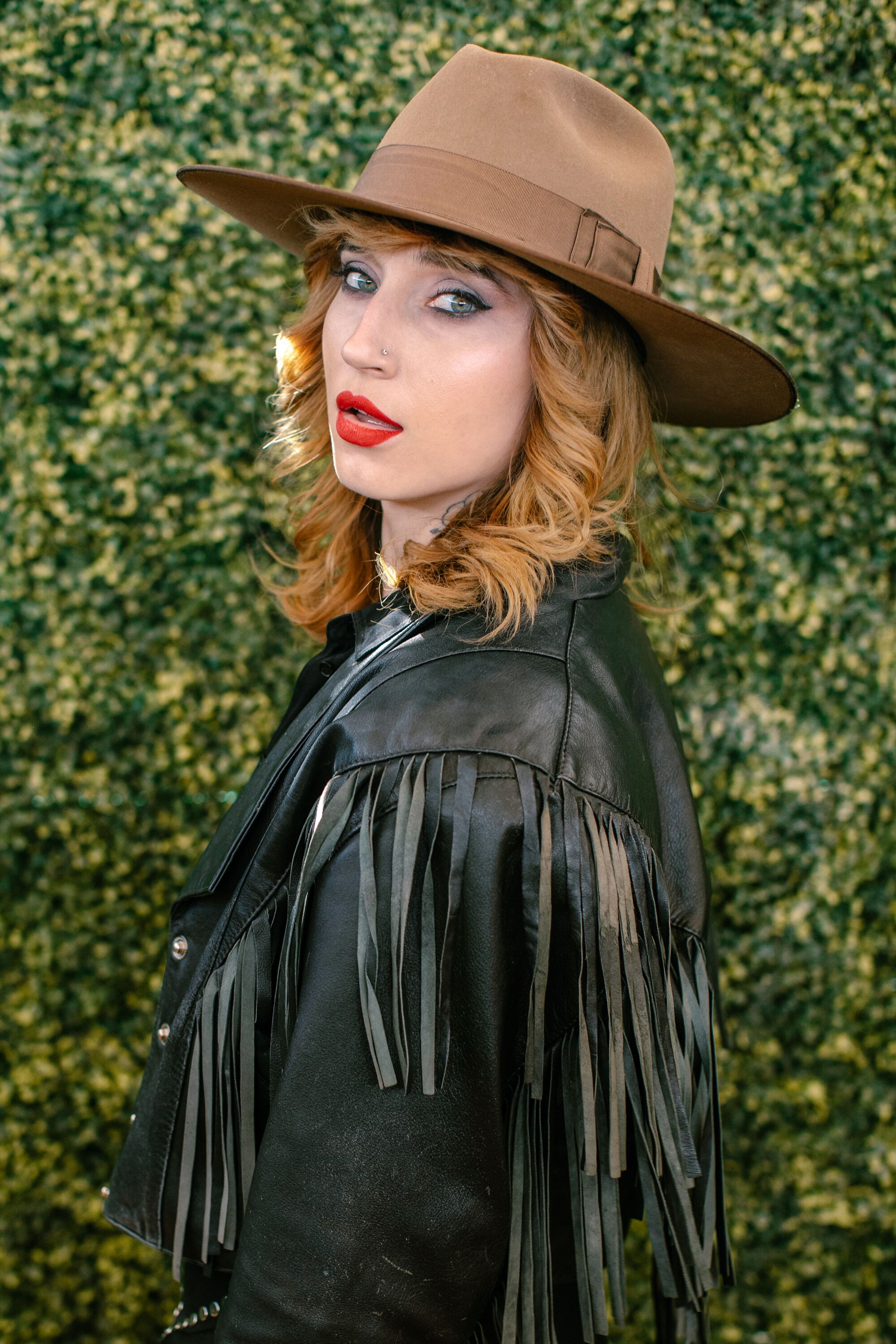 A red-haired woman in a black fringed jacket and a brown hat.