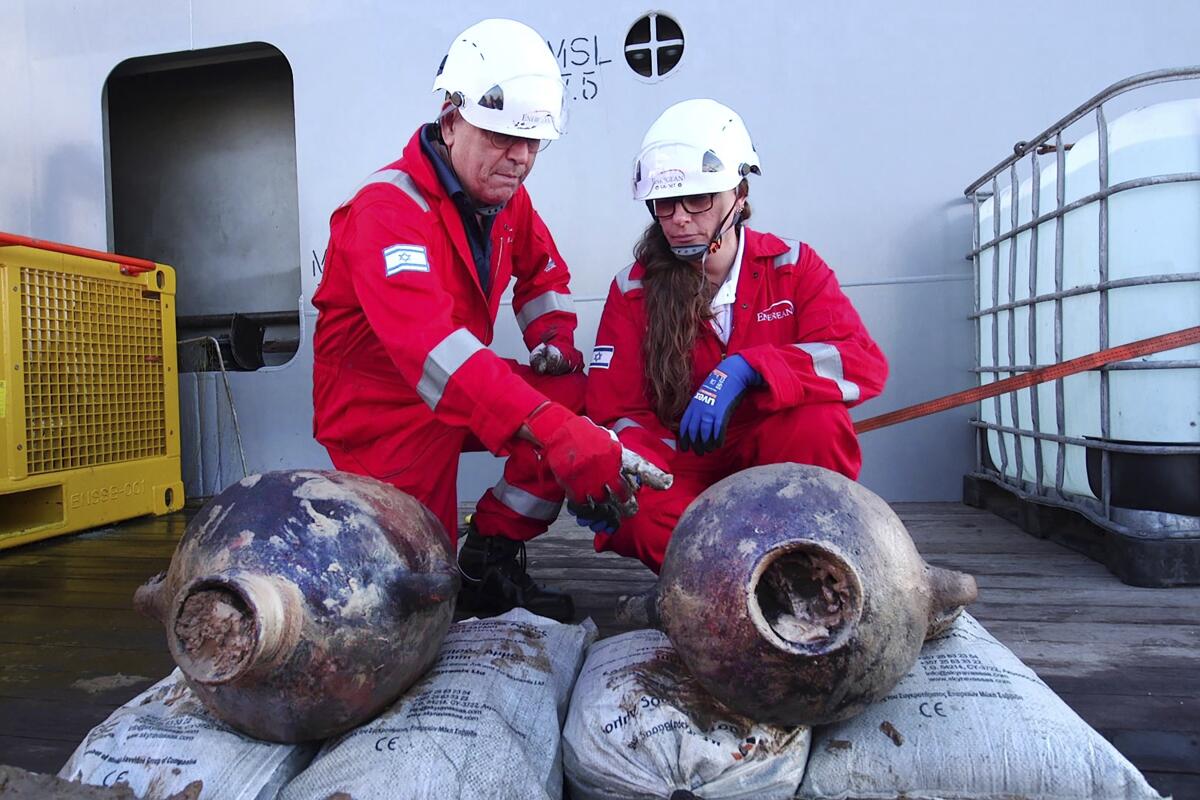 men in hard hats with the ancient jars that were carried on the world's oldest known deep-sea ship.