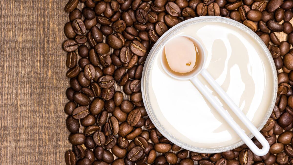 Cellulite busting product concept. Anti-cellulite cosmetics with caffeine. Jar of cream with a spoon of coffee essential oil surrounded by coffee beans on wooden surface. Top view. Copy space ** OUTS - ELSENT, FPG, CM - OUTS * NM, PH, VA if sourced by CT, LA or MoD **