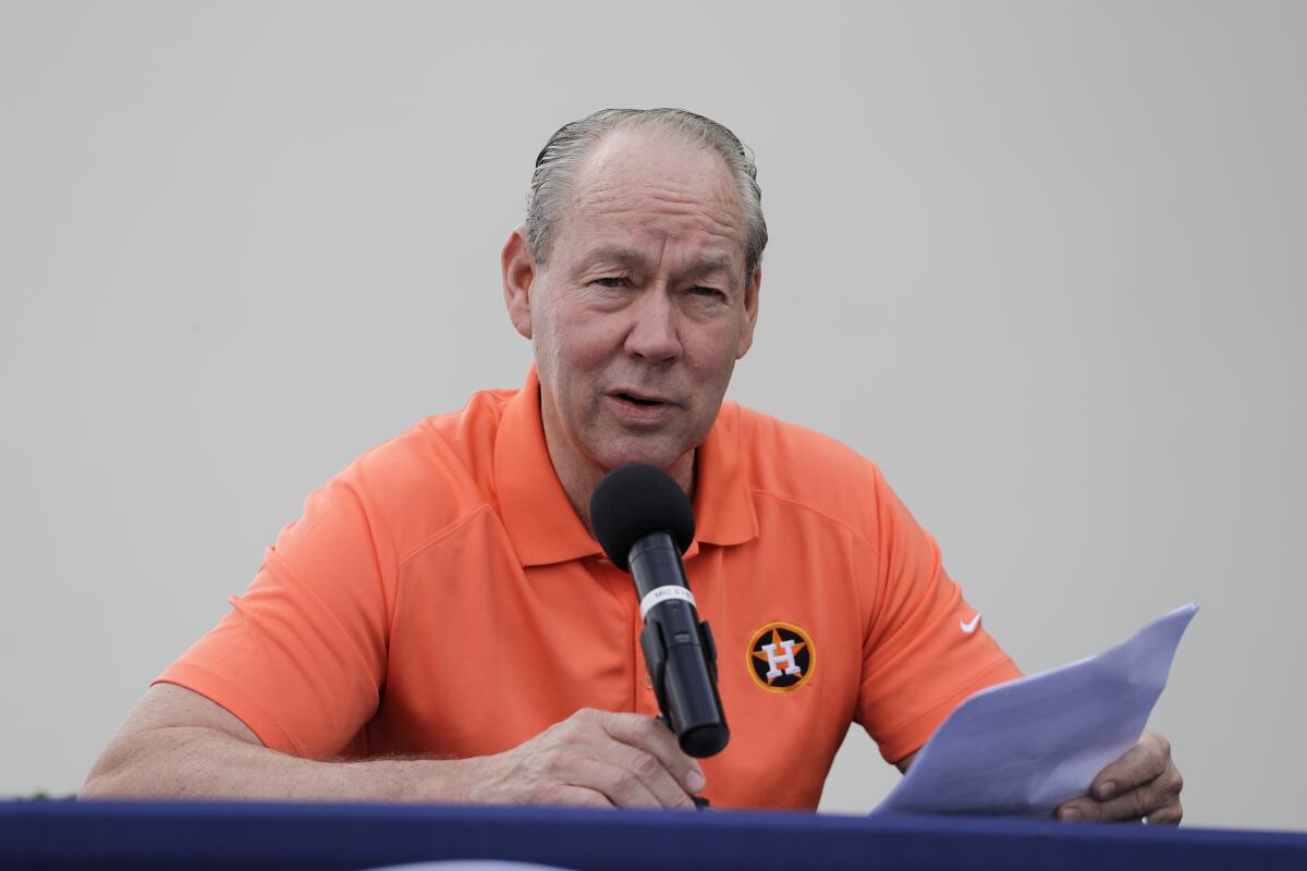 Houston Astros owner Jim Crane speaks at a microphone while holding papers.