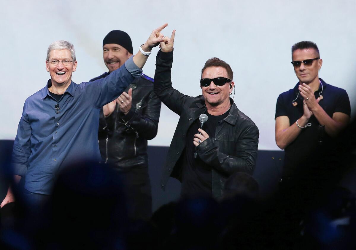 Apple CEO Tim Cook, left, greets the crowd with U2 singer Bono, second from right, as The Edge, second from left, and Larry Mullen Jr. look on during an Apple special event in Cupertino, Calif.