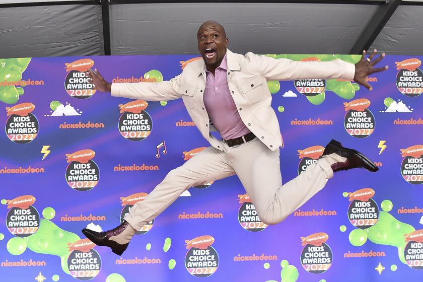 A Black man in a white suit leaps through the air as he arrives at an awards show