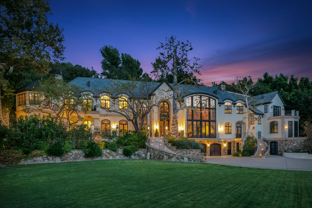 The front of a mansion with a two-story entrance and large windows, sitting on an expansive lawn.