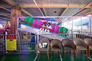 A woman and a child sit at an angle on a ride with pink and green seats