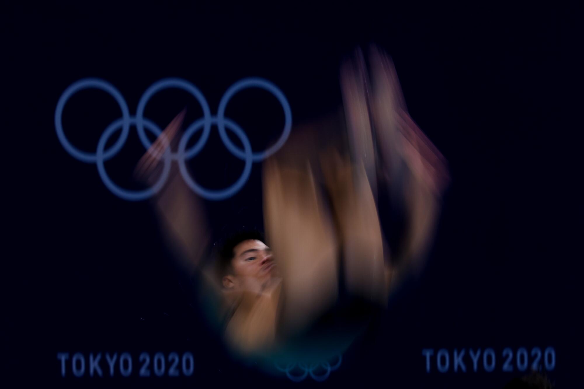 A man's face is clear and the rest of his body a blur, with the Olympic rings in the background.