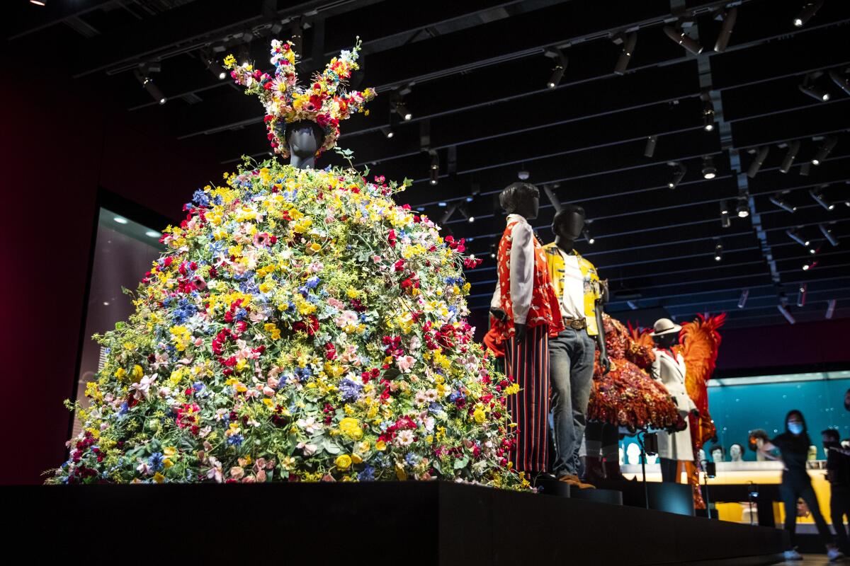 A massive dress made of fake flowers is on display on a low-rise museum plinth.