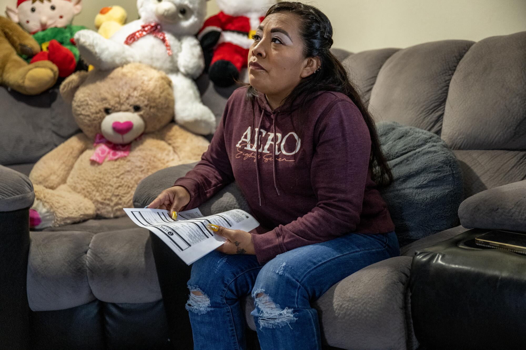 A woman holds a sheet of paper as she sits on chair near plush toys.