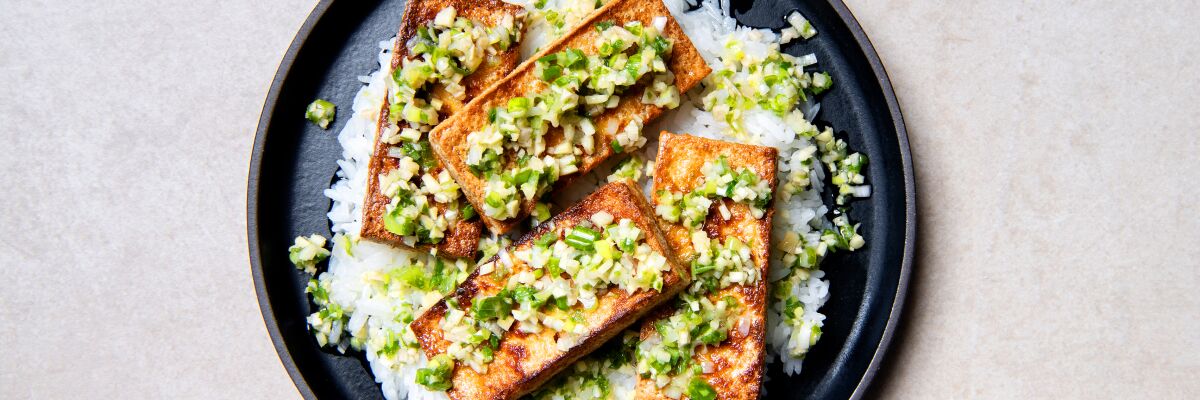 Four slabs of pan-seared tofu with sizzling ginger-scallion sauce over a bed of steamed, white rice.