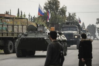Syrian fighters watch Russian armored vehicles driving past near Hmeimim Airbase.