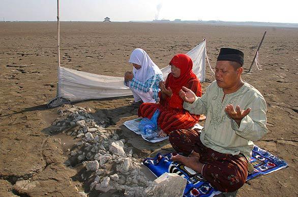 Members of a family pray at a place where they believe their house once stood before it devastated by a mudflow two years ago near Porong, Indonesia. Muslims around the world have begun celebrating Eid al-Fitr, the three-day festival that marks the end of the Ramadan month of fasting.