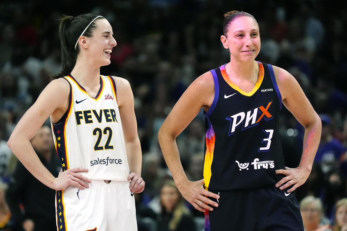 Caitlin Clark and Diana Taurasi hold their hands on their hips and smile.