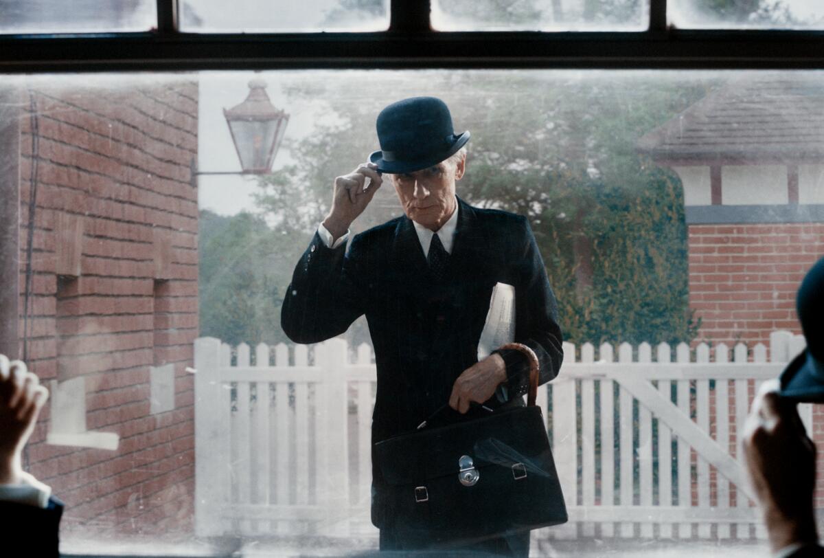 An old man in a suit tips his bowler hat.