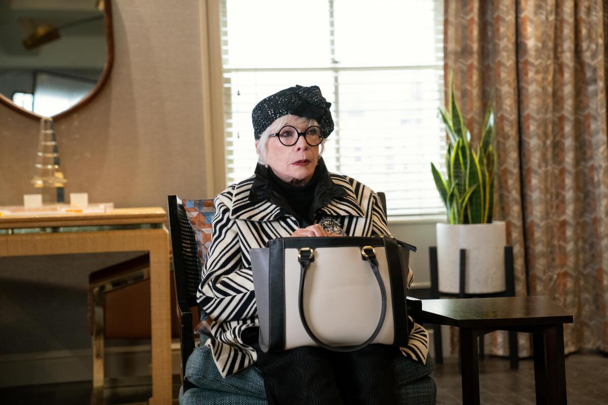 An affluent older woman in a black-and-white outfit sitting with a black-and white purse on her lap