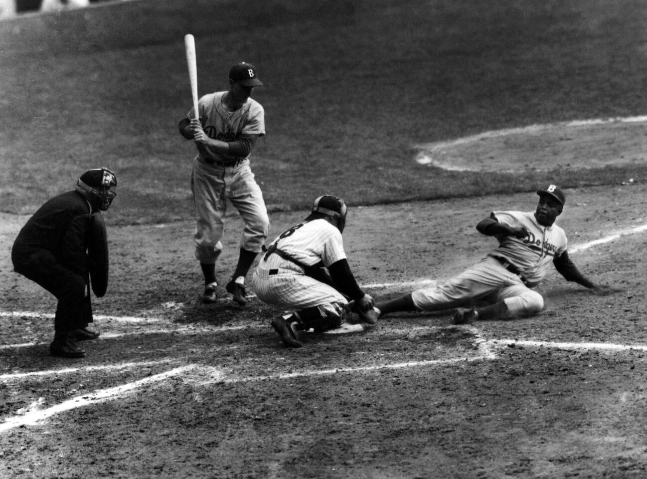 Jackie Robinson safely steals home under the tag of Yankees catcher Yogi Berra in the eighth inning of the 1955 World Series opener at Yankee Stadium. The Dodgers would win the championship in seven games, the first in franchise history and only title for Brooklyn.