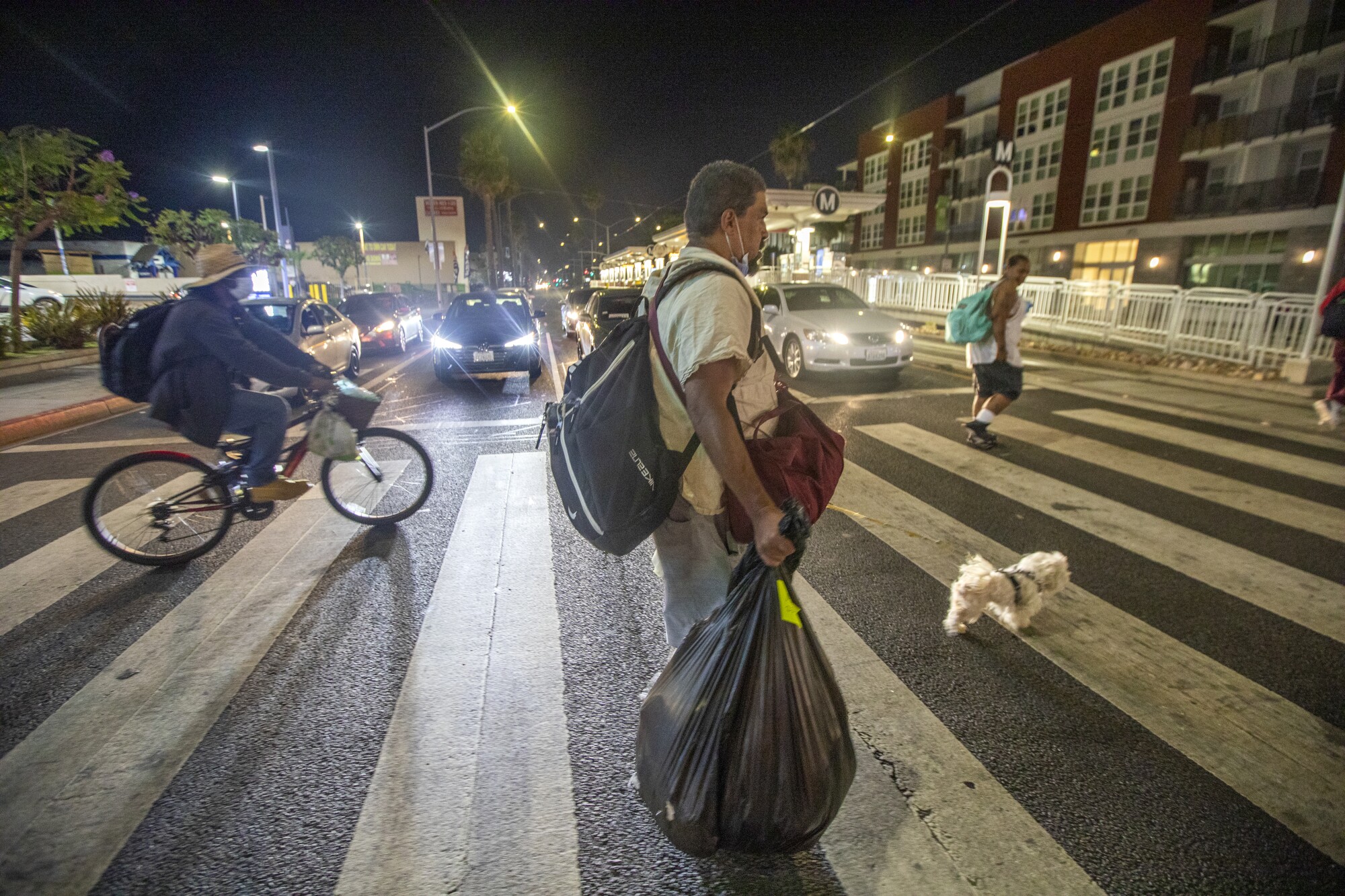 A man crosses an intersection carrying a garbage bag