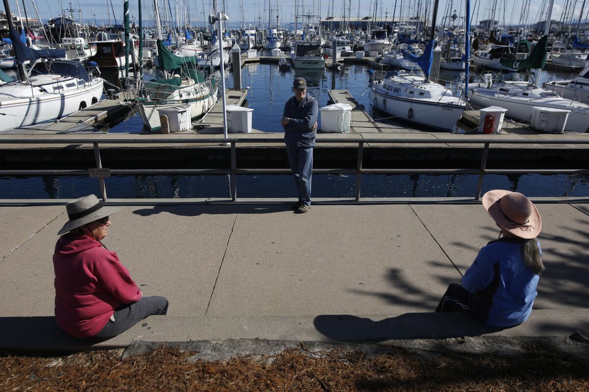 Terry Hanna, left, her husband, Mike, and Melanie Cervi practice social distancing Tuesday near Fisherman's Wharf in Monterey, Calif.