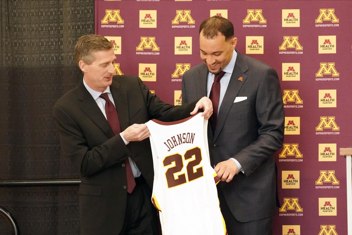 Minnesota athletic director Mark Coyle presents a jersey to men's basketball coach Ben Johnson during a news conference.