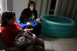 Two women sit, each holding a child in their lap