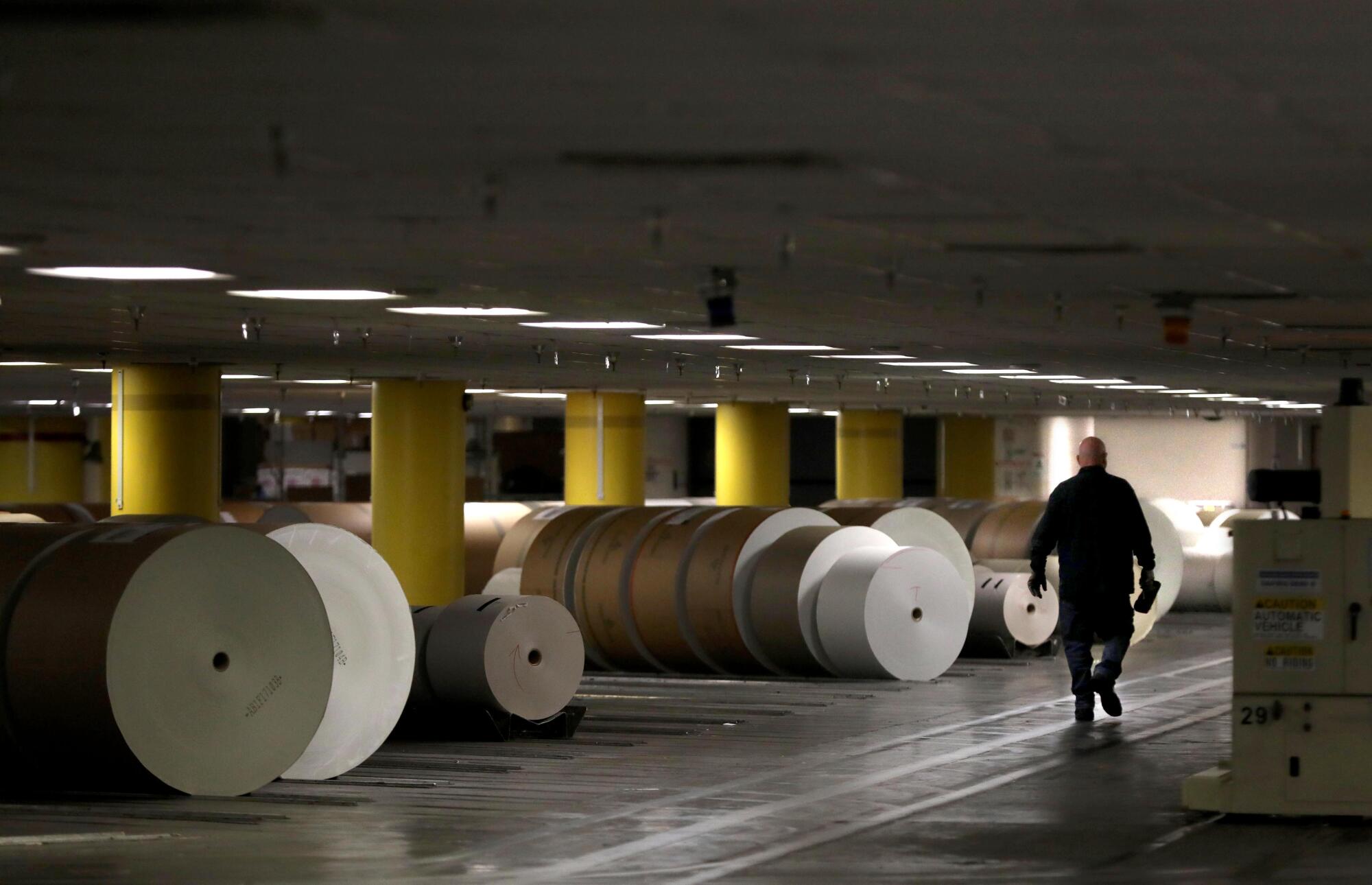 A man walks by remaining rolls of paper at the Olympic printing plant in Los Angeles