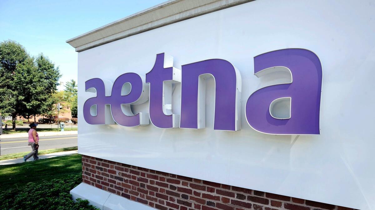 A pedestrian walks past a sign for Aetna Inc., at the company headquarters in Hartford, Conn.