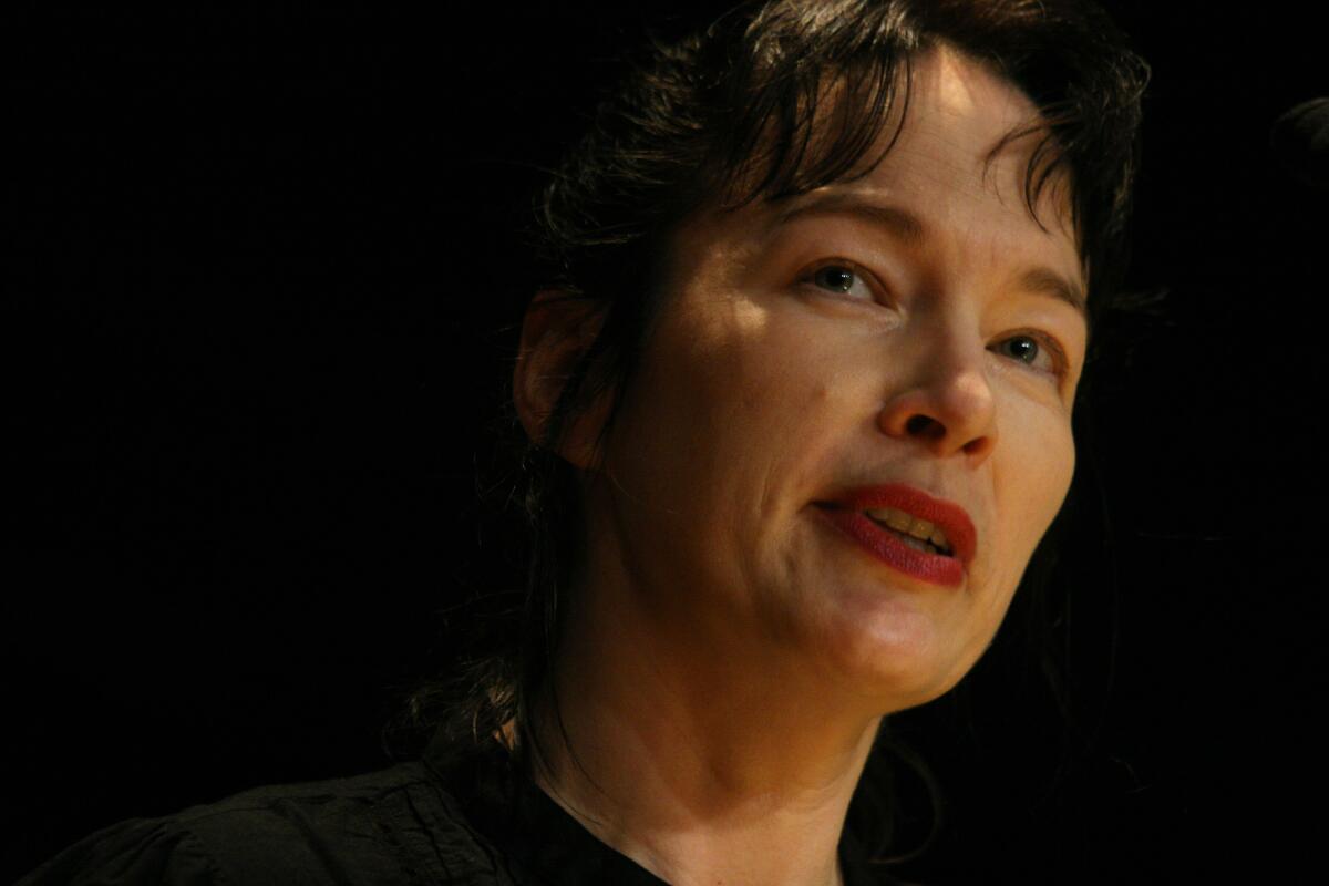 A woman with dark hair speaks in front of a dark background.