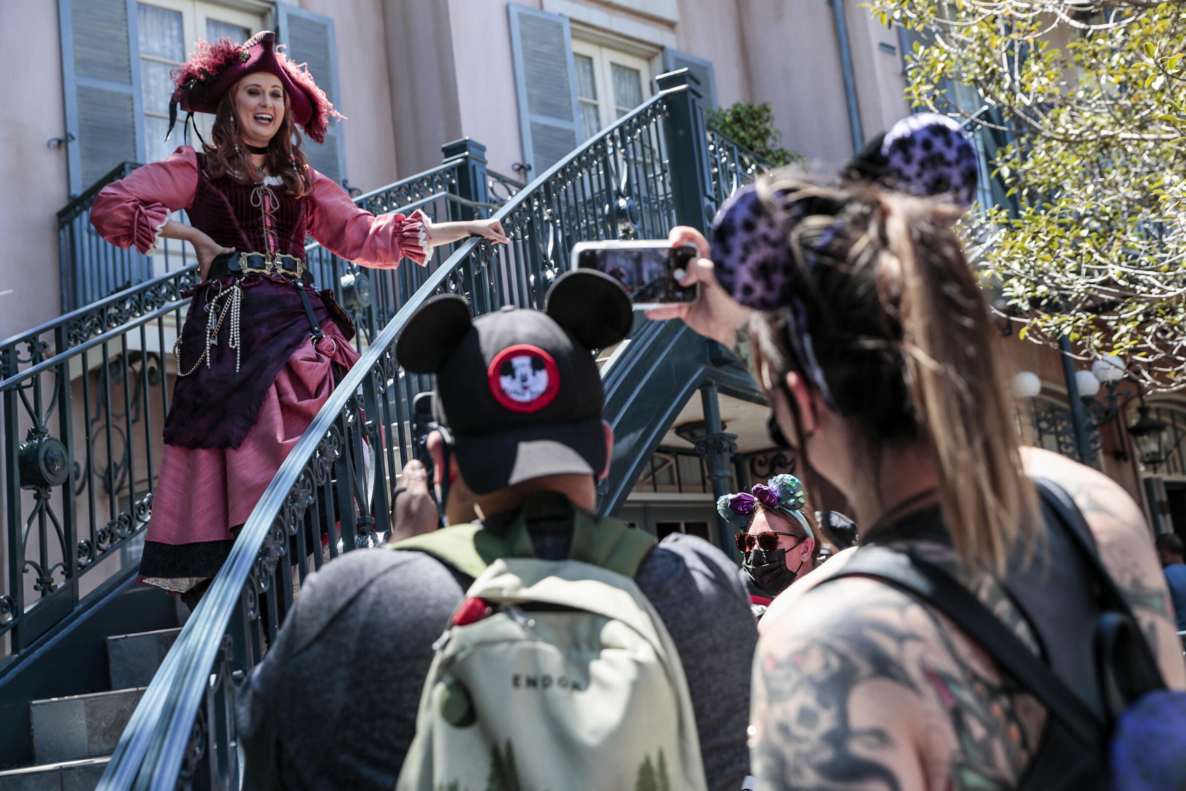 A woman in a pirate costume chats with people wearing mouse ears  