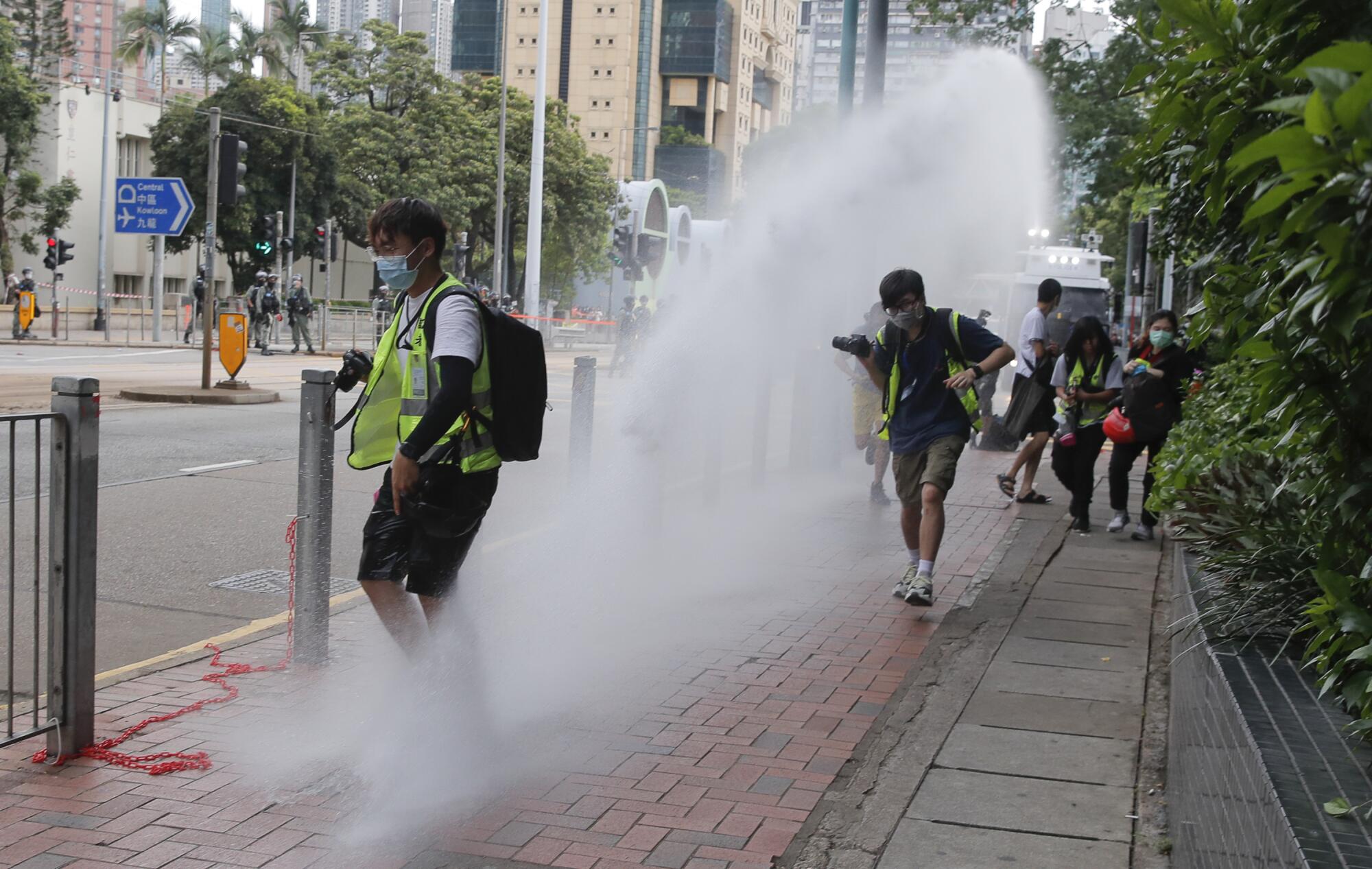 Journalists run as police fire water cannons during a demonstration against the new national security law in Hong Kong.