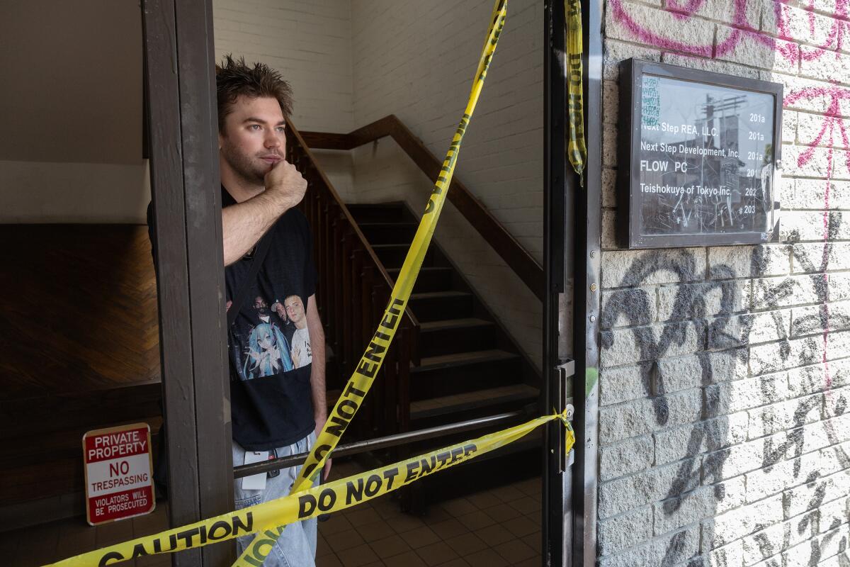 A man in a black T shirt stands in a doorway behind caution tape.