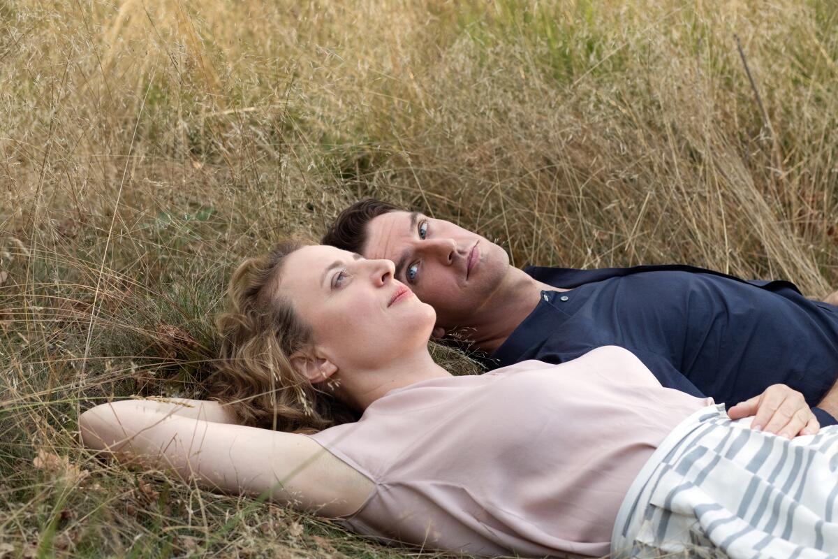 A man and a woman lie side by side on their backs in the grass.