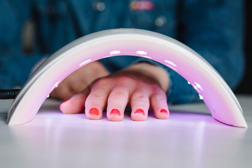 Woman holds her hand inside a UV lamp to dry the gel nail polish that was just applied..