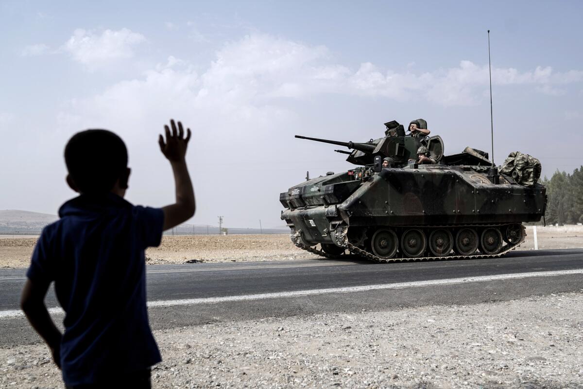 A child waves toward Turkish troops heading to the Syrian border, in Karkamis, Turkey, Friday, Aug. 26, 2016.