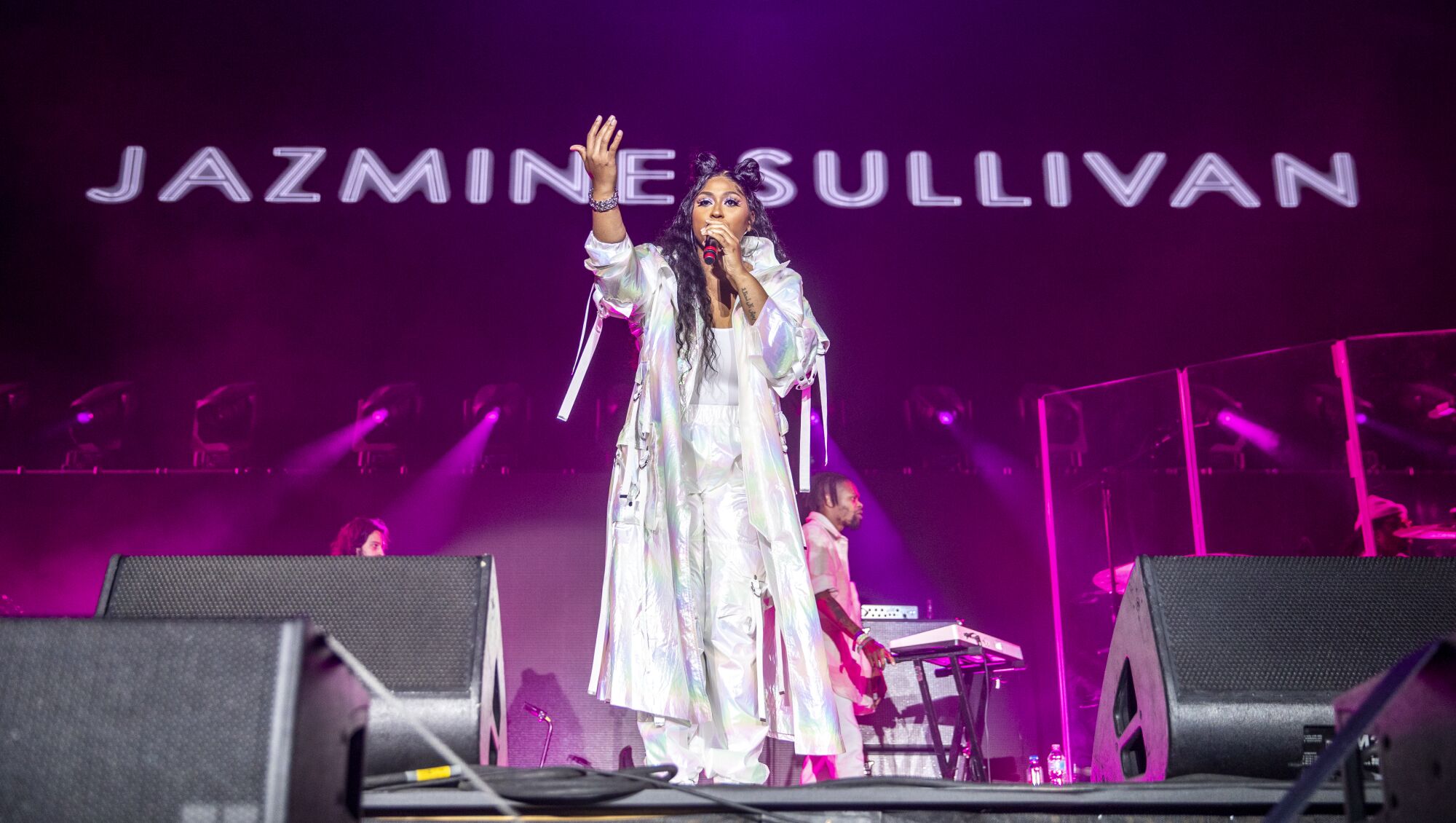 Jazmine Sullivan raises an arm while performing on a stage with her name above the stage.