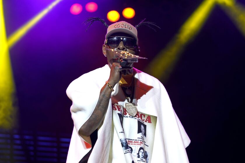 Coolio in a white t-shirt wearing sunglasses and holding a microphone to his mouth
