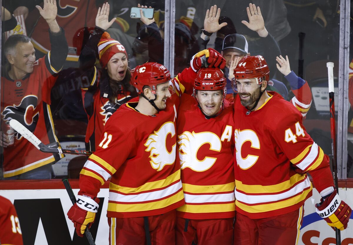 Calgary Flames' Matthew Tkachuk, center, is congratulated by Mikael Backlund, left, and Erik Gudbranson after Tkachuk scored against the Vegas Golden Knights during the third period of an NHL hockey game Thursday, Feb. 9, 2022, in Calgary, Alberta. (Jeff McIntosh/The Canadian Press via AP)