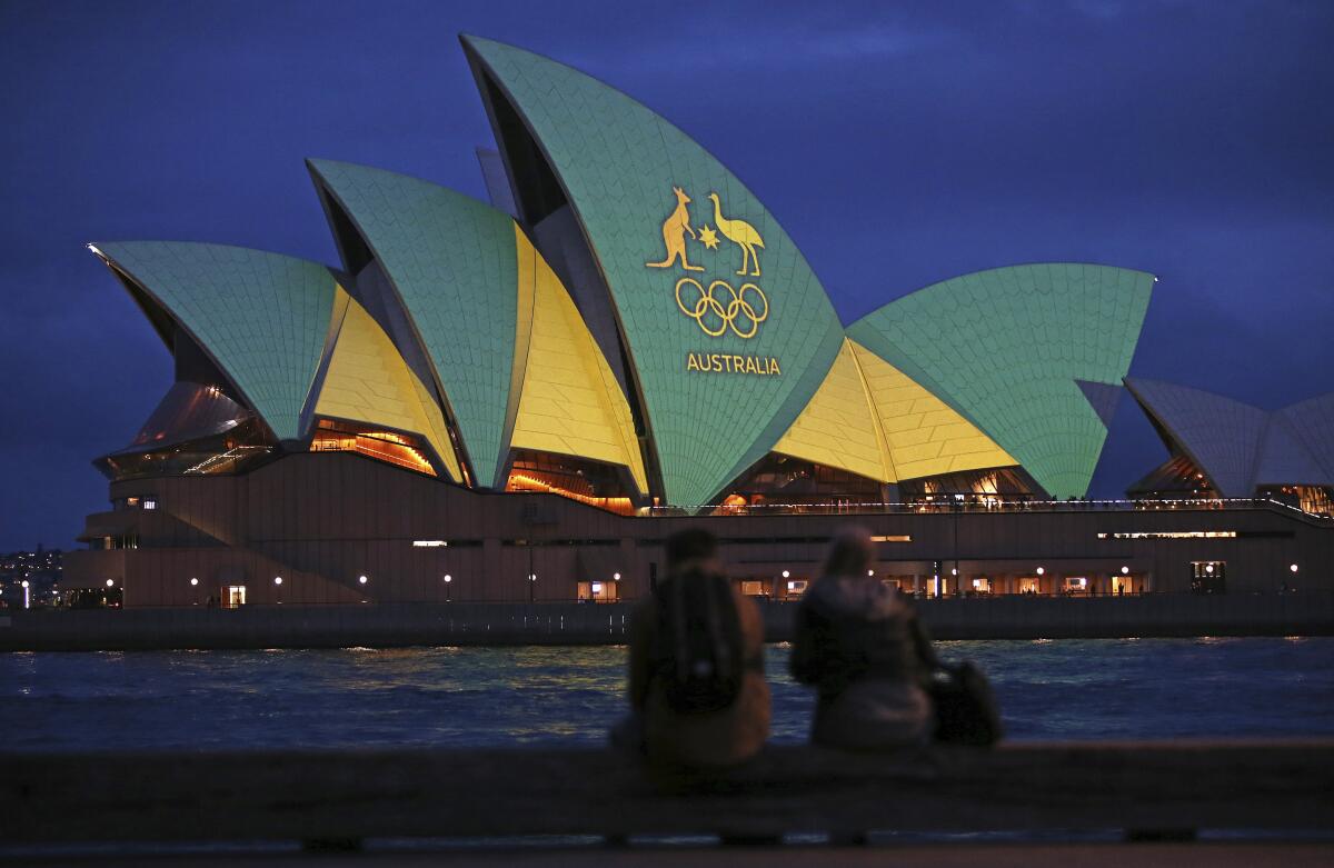 FILE - In this Friday, Aug. 5, 2016, file photo, a couple sit on a dock to look at the sails of the Sydney Opera House that are illuminated with the green and gold colors of the Australian Olympic team, as Australia pushes to host the 2032 Olympics. Brisbane will be offered as the 2032 Olympics host, IOC president Thomas Bach said Thursday June 10, 2021, for International Olympic Committee members to confirm in Tokyo next month. (AP Photo/Rick Rycroft, File)