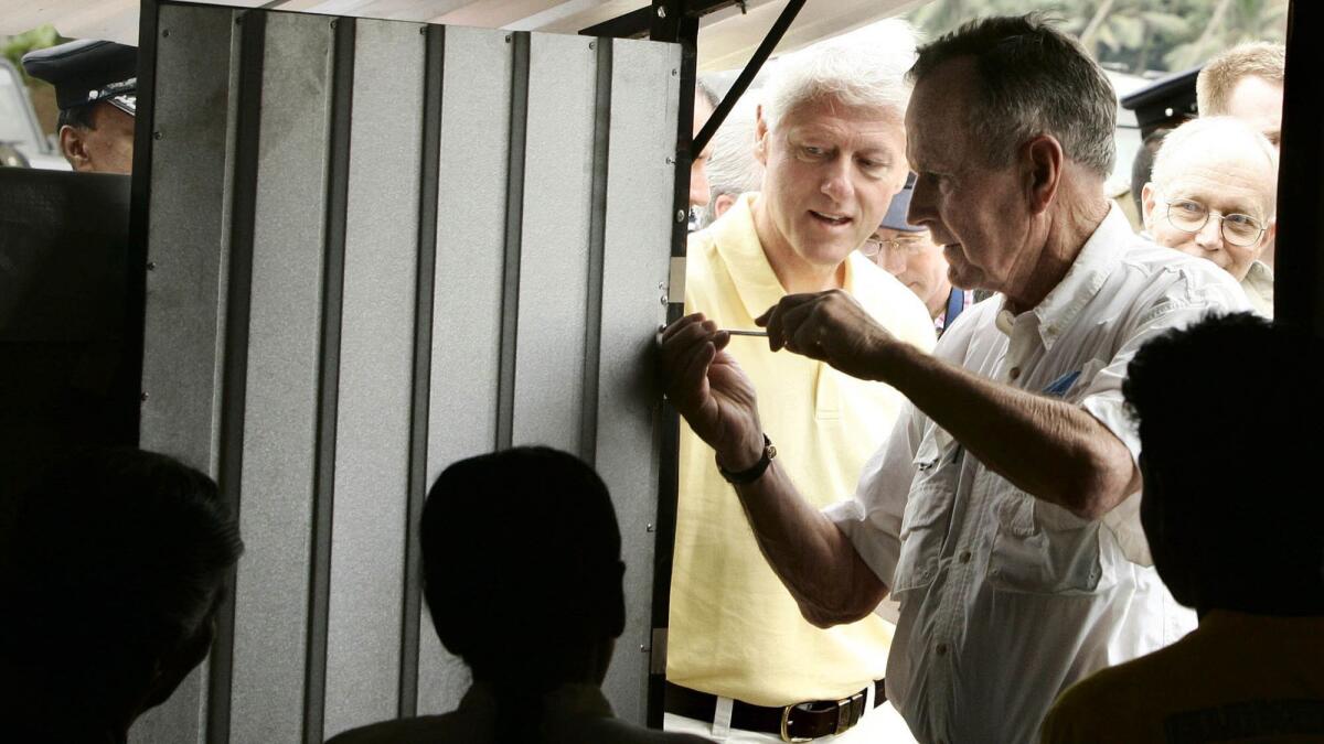 George H.W. Bush puts the final screw in a temporary home during a February 2005 visit that included Bill Clinton, center, to displaced tsunami victims in Weligama, Sri Lanka.