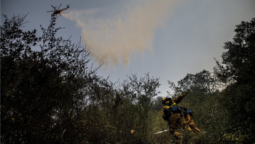 Firefighters work on clearing brush while a helicopter makes a water drop on a Thomas fire hot spot in the Santa Ynez Mountains.