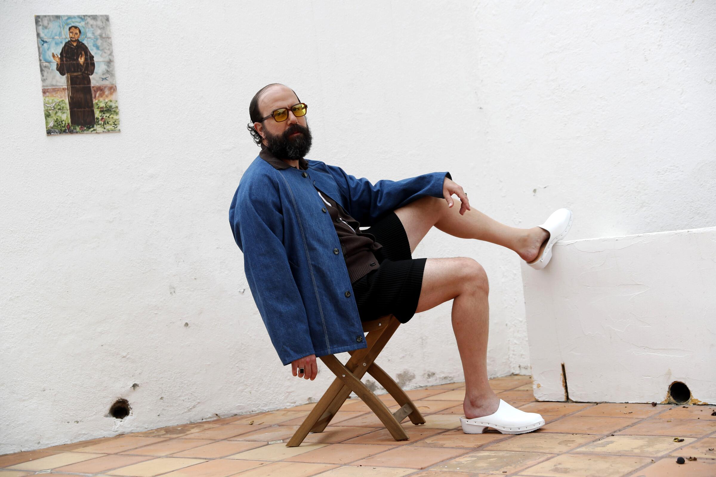 A man in a denim shirt and shorts leans back in a chair on his patio