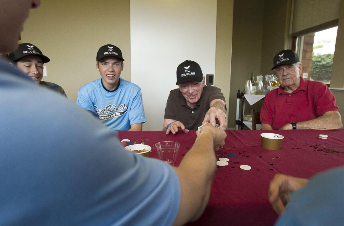 Corona del Mar High baseball players Caden Campbell, left, and Tanner Ivey watch as Ed Isenberg cuts the cards for CdM’s Chase Hartsell during a game of 21 at the Crown Cove assisted living facility on Saturday. Also in the photo is resident Bob Simpson. The baseball players’ OC Silvers group visits with the seniors at the facility.