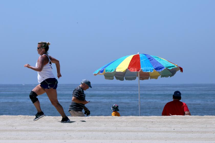 A woman runs on the sand as others take in the sights on the beach next to the Balboa Pier in Newport Beach on Wednesday, May 6, 2020. The city partially opened the beaches under an "active recreational use" plan approved today by State officials.