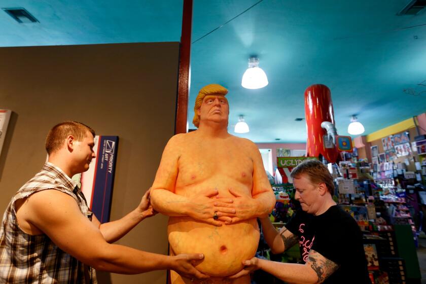 Robert Crichton, left, and Matt Kennedy move a statue depicting a nude Donald Trump back outside to the entrance of Soap Plant Wacko in Los Feliz.