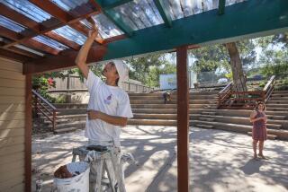 Painter Alder Flores applies finishing touches to an awning at the outdoor amphitheater of the new middle school campus of The Rhoades School in Encinitas. At right is Regina McDuffie, the school's director.